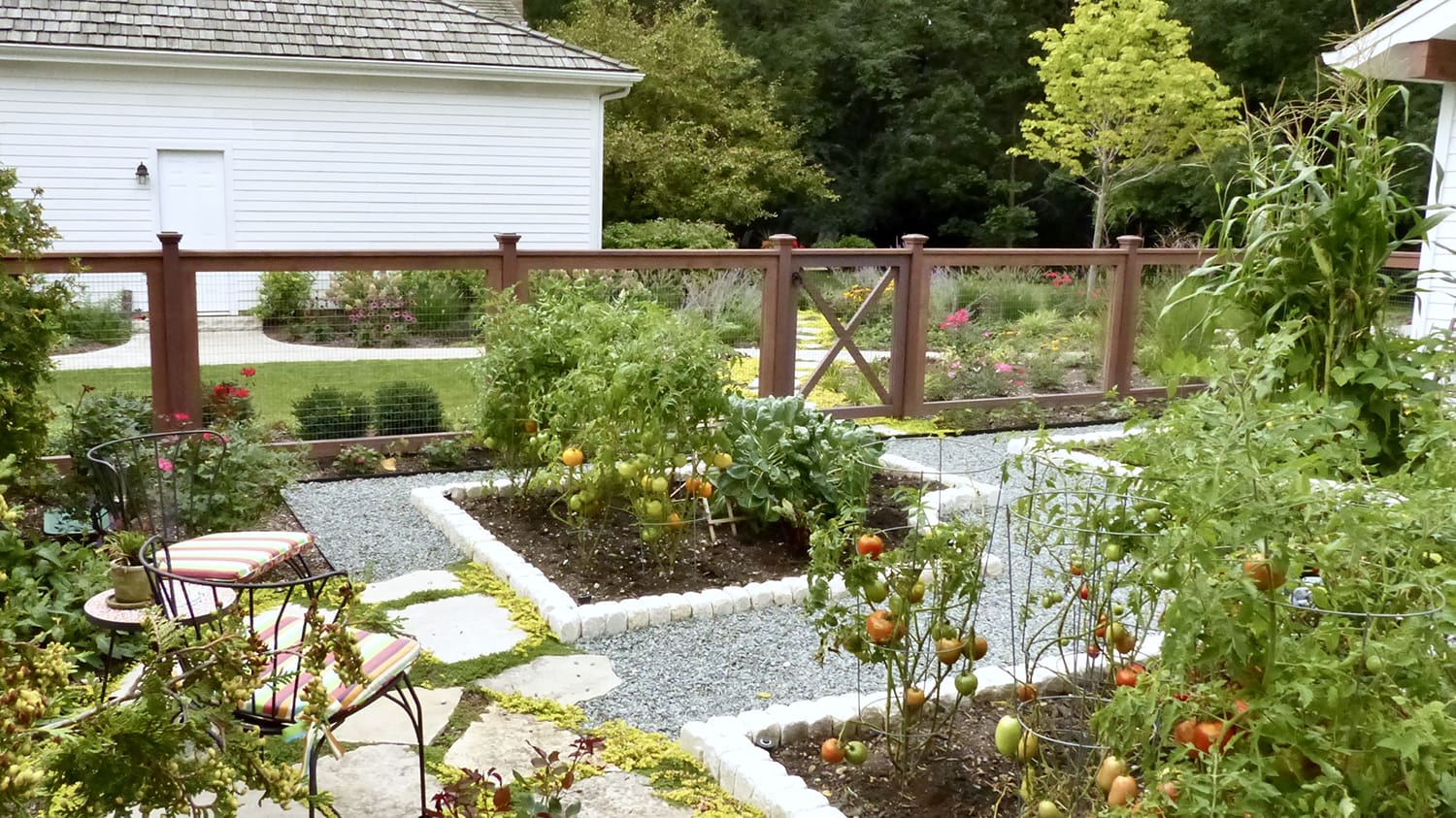 Tomato beds and vegetables growing inside a fenced garden with small seating area in Green Oaks