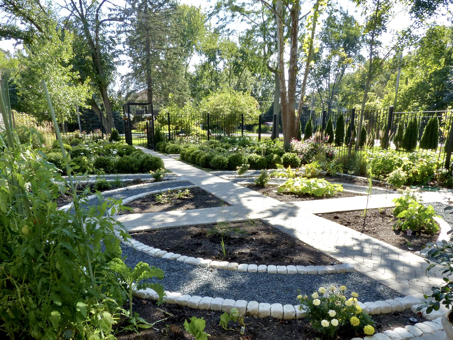 Vegetable garden with curved gravel paths, raised plant beds, and formal hedges in a Riverwoods garden