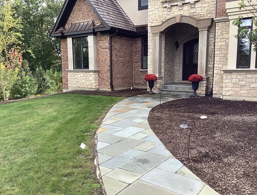 Before renovation view of a front yard in Kildeer, Illinois, showing minimal landscaping, curved stone walkway, and undeveloped planting beds.